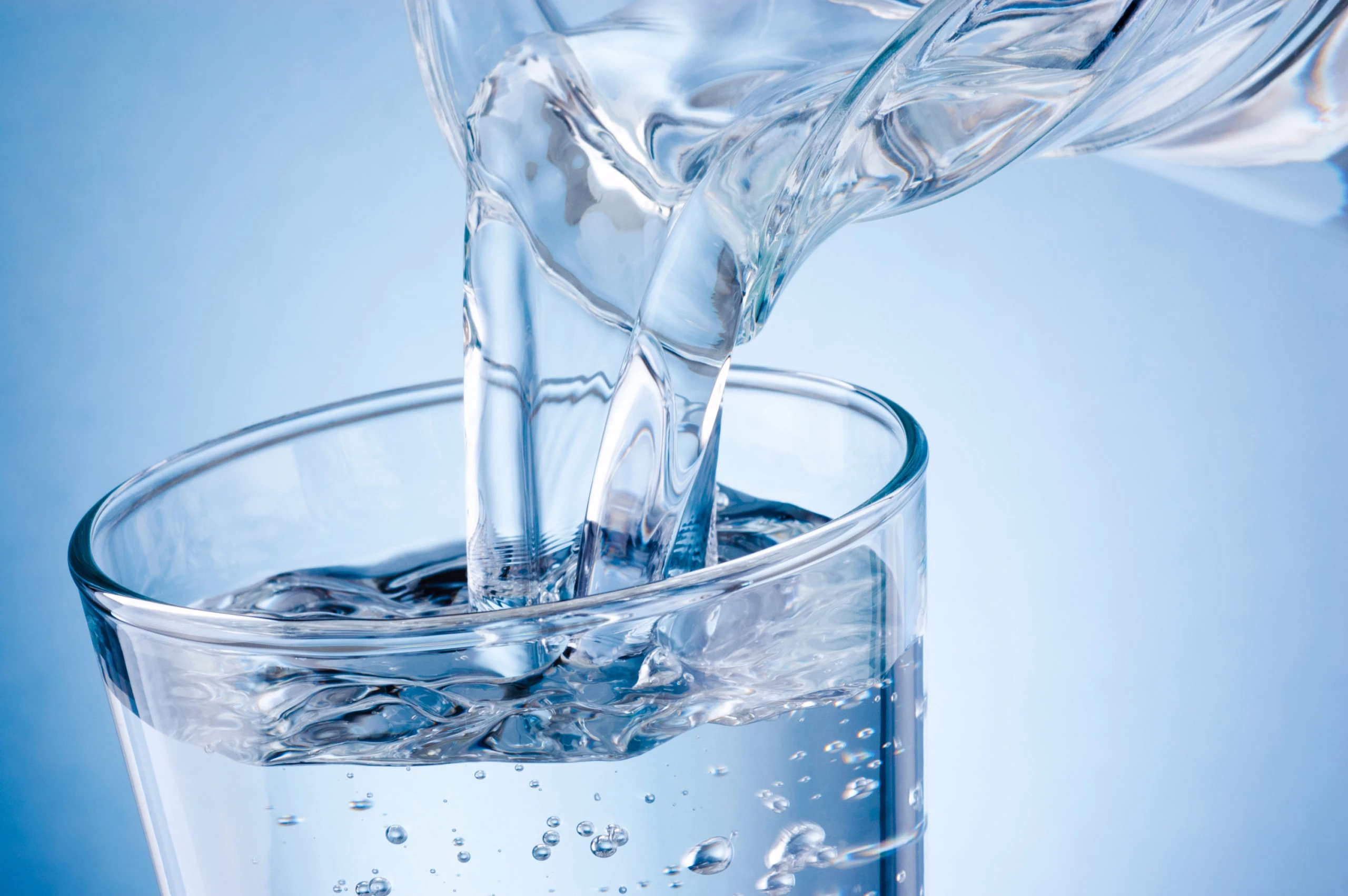 Pouring water from jug into glass on blue background Potable Water